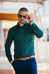 Canvas Print - Cool handsome Caucasian man wearing an elegant green shirt and sunglasses posing outdoor