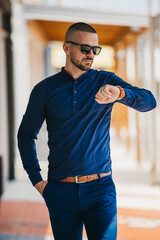 Wall Mural - Cool handsome Caucasian man wearing an elegant blue shirt and sunglasses posing outdoor