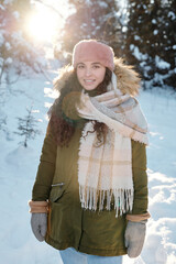 Wall Mural - Happy young female in winterwear standing in the forest on sunny winter day