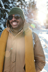 Wall Mural - Happy young African guy in winterwear and sunglasses chilling in winter forest