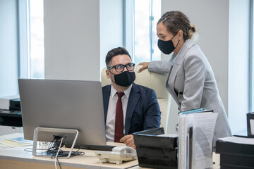 Aufkleber - Young businesswoman and her colleague in protective masks computing and interacting by workplace