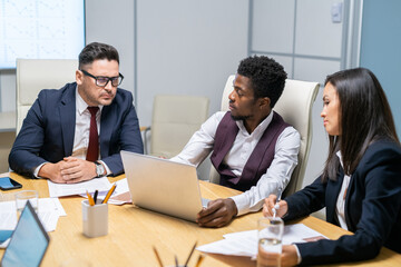 Poster - Confident African businessman with laptop making presentation while mature coach looking at display