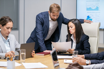 Poster - Young businesswoman showing financial papers to her male colleague among other office workers