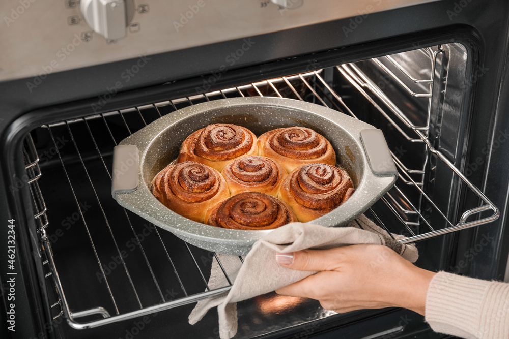 Woman taking tasty cinnamon rolls from oven in kitchen