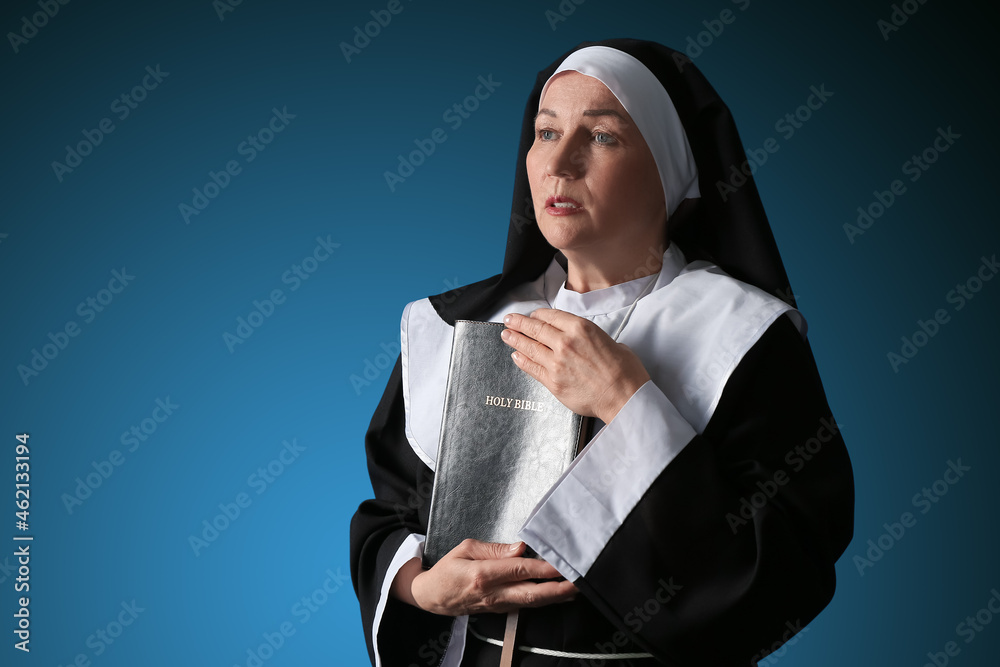 Mature nun with Holy Bible on color background