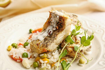 Plate with tasty baked cod fillet, rice and vegetables on table in restaurant, closeup