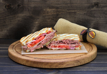 Roast beef panini with tomato, onion and cheese on a round cutting board