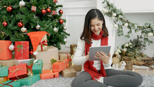 Asian Woman Using Smart Tablet Sit At Christmas Tree Xmas Present Gift Box In Cozy Living Room. Woman Hand Touch Screen Smile Shopping Online, Happiness Time Christmas Holiday Winter Season Festive