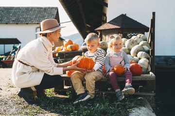 Mother with children are choosing pumpkin in farm market. Woman and little kids playing on fall walk at countryside. Thanksgiving holiday and Halloween. Happy Family at Autumn season.