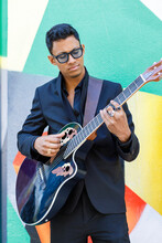 Male Musician Playing Guitar While Standing In Front Of Colorful Wall