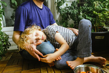 Son Resting Head On Father's Lap While Sitting Near Plants In Balcony