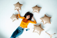 Smiling Woman Amidst Star Balloons Lying On Floor At Home