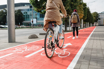 traffic, city transport and people concept - woman cycling behind pedestrian walking along red bike lane on street in tallinn, estonia