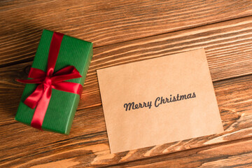 Canvas Print - top view of greeting card with merry christmas lettering near wrapped green present on wooden surface