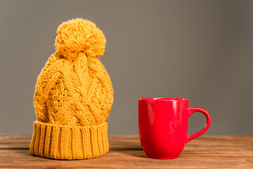 Canvas Print - red cup of tea near knitted hat on wooden surface isolated on grey