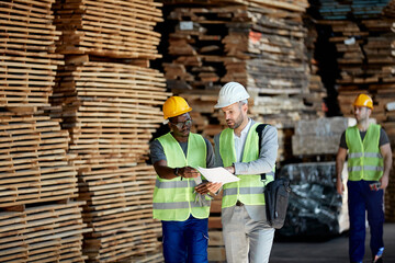 Young black worker and inspector go through paperwork while walking through warehouse.