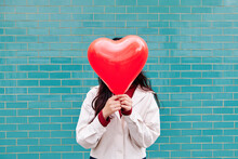 Woman Covering Face With Red Heart Shape Balloon