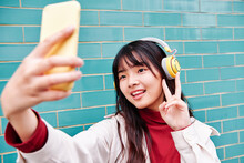 Woman Showing Peace Sign While Taking Selfie In Front Of Turquoise Brick Wall