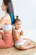 © Вадим Каштанов - Young woman and toddler girl sit in lotus position back to back on rug. Morning yoga practice. toddler girl looking camera.