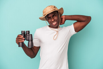 Wall Mural - Young African American man holding binoculars isolated on blue background touching back of head, thinking and making a choice.