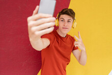 Man With Headphones Showing Peace Sign While Taking Selfie In Front Of Wall