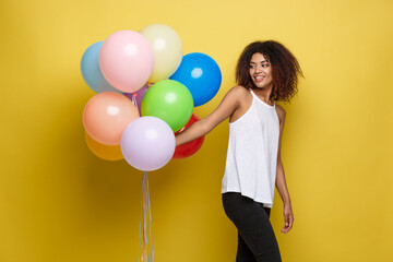 Wall Mural - Celebration Concept - Close up Portrait happy young beautiful african woman with white t-shirt smiling with colorful party balloon. Yellow Pastel studio Background