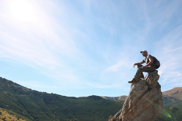 Wall Mural - Man with backpack on rocky peak in mountains. Space for text