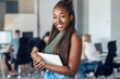 © nenetus - Smiling young entrepreneur woman using her digital tablet while standing and looking at camera in a coworking place.