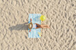 © New Africa - Woman sunbathing on beach towel at sandy coast, aerial view