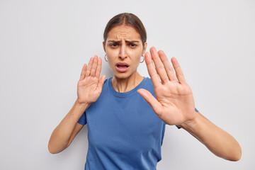 Do not come closer. Displeased woman shows her denial opinion says stay away from me calm down or slow asks to keep distance demonstrates taboo gesture dressed casually isolated over white wall