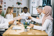 © Sofiia Shunkina - Team of mixed race doctors sitting at table on conference room and sharing with reports during medical research. Male and female therapists cooperating for common success.