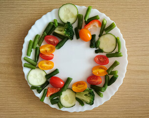 Fresh Organic Vegetables on wooden Table Around White Plate with copy space for your text. Cherry tomatoes, peppers, cucumber slices, broccoli and green beans