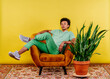 © VISTA by Westend61 - Young man sitting on armchair by plant