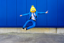Man Wearing Vibrant Blue Suit And Bird Mask Jumping Against Blue Wall