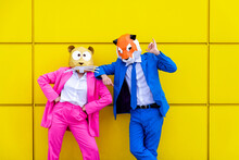 Man And Woman Wearing Vibrant Suits And Animal Masks Posing Together Against Yellow Wall