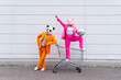 © VISTA by Westend61 - Man and woman wearing vibrant suits and animal masks posing with shopping cart and disco ball in front of white wall