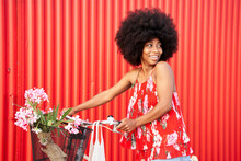 Afro Woman With Bicycle Smiling While Standing By Red Wall
