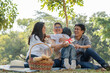 © Supachai - Happy Asian family grandson hugging and giving gift box to grandmother while picnicking in the park