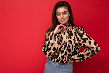 Wall Mural - Image of a beautiful young brunette woman dressed in animal printed blouse posing isolated over red background with copy space