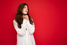 Portrait Of Beautiful Young Curly Brunette Woman Wearing White Shirt Isolated On Red Background With Free Space, Wanting And Dreaming With Sincere Emotions