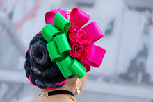 Closeup Of Rear View Of Hispanic Dancer's Headress And Hairdo In Bright Pink And Green Against Blurred Background.