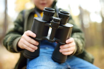 Wall Mural - Little boy scout with large binoculars during hiking in autumn forest. Child is looking through a binoculars. Concepts of adventure, scouting and hiking tourism for kids.