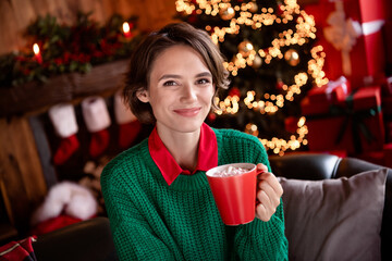 Photo of shiny cute young lady wear green pullover smiling drinking tasty beverage indoors house home room