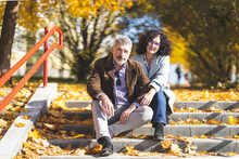 Man And Woman Posing While Sitting On Concrete Steps. Portrait Of A Mature Couple 50 Years Old In An Autumn Park.