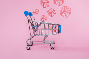 blue shopping cart with red percentage signs on cubes on pink background, retail and discount concept