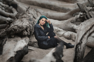 Wall Mural - beautiful woman with blue hair sits on the sand on the beach surrounded by log trees