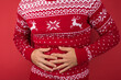 Cropped closeup photo of man in red and white christmas sweater holding his hurting stomach on isolated red background