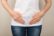 © ActionGP - Cropped closeup photo of young woman in white t-shirt and jeans holding her hands on lower abdomen on isolated grey background