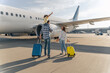 © Yaroslav Astakhov - Back view of happy family standing near a large plane with two suitcases outdoor. Trip concept