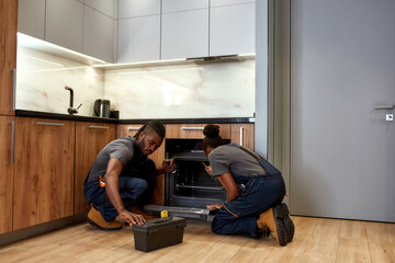 Experience and knowledge exchange concept. Expert and apprentice fixing kitchen oven